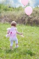 little girl with pink balloons on the meadow