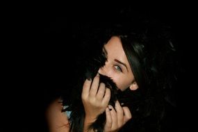 portrait of green-eyed girl with black hair enfolding in feathers