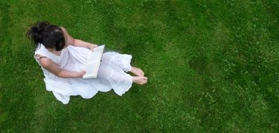 girl reading book on green grass