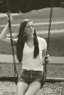 black and white photo of a girl on a chain swing