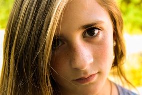 portrait of a girl with freckles and long hair at blurred background with the plants and light