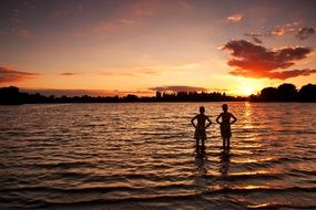 children stand in the water and watch the sunset