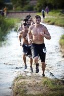 group of young male athletes running through water and mud