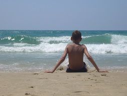 dark skin boy sitting on beach, back view