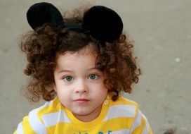 blue-eyed child with curly hair with a headdress of ears of Mickey Mouse