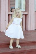 a little girl in a white dress standing on the steps