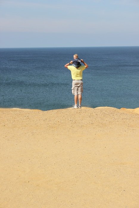 father carries baby on his shoulders at the beach