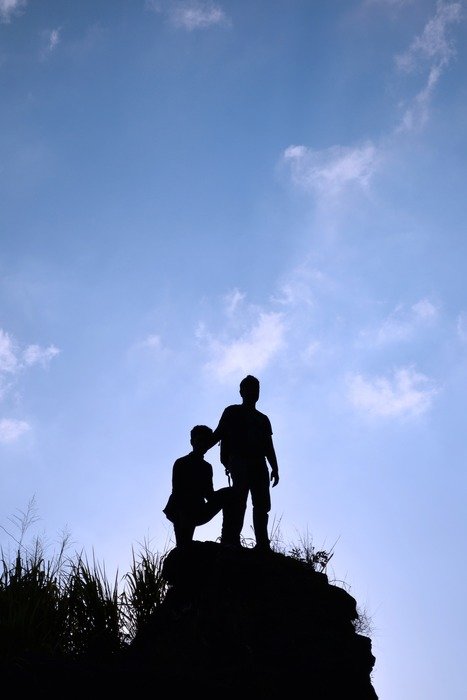 silhouette of guys on a high rock