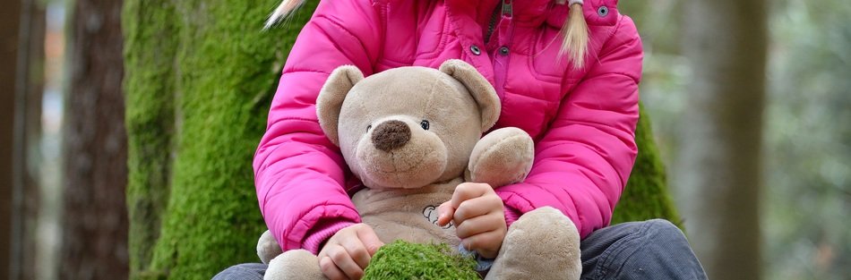 photo of child with teddy bear in a forest
