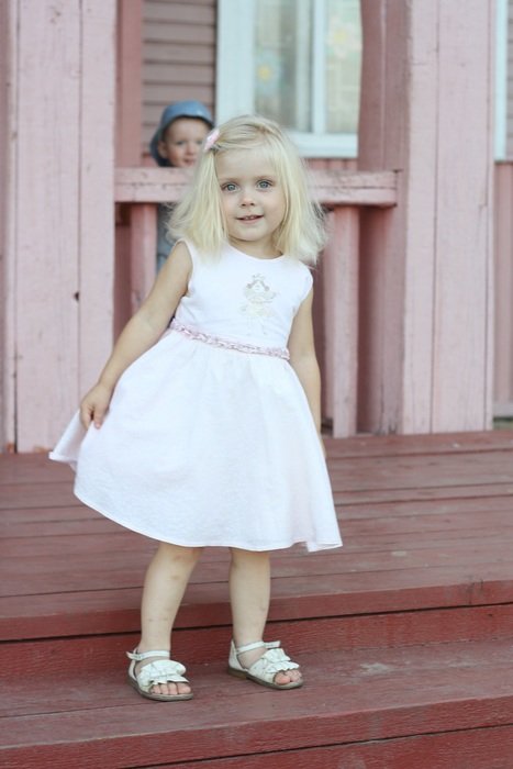 a little girl in a white dress standing on the steps