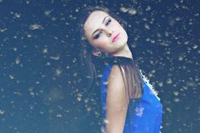 portrait of Beauty girl in a blue dress on a background of snowflakes and flying feathers