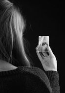 Black and white photo of girl looking at small mirror