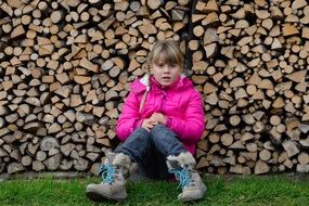 Pretty girl blond sit on green grass and wooden logs