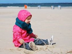 warmly dressed little girl sitting on the beach