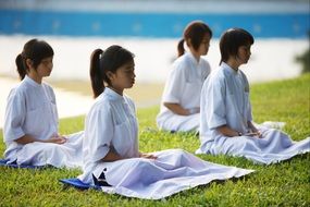 buddhists, four school girls meditating on lawn