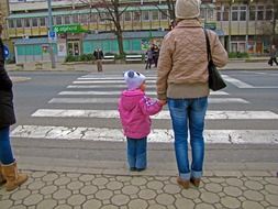 mom and daughter are waiting near the crosswalk to cross the road