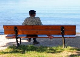 an old man sits on a bench by the river