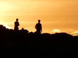 two men silhouettes at golden sky