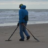 young man with a metal detector and shovel on the sandy coast