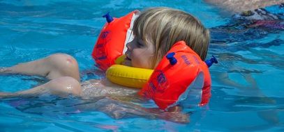 blond child girl in swim ring on water