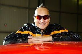 man with glasses near a red car