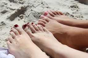 women's feet with red and pink pedicure lie on the sand