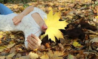 girl lying on autumn grass with yellow maple leaf