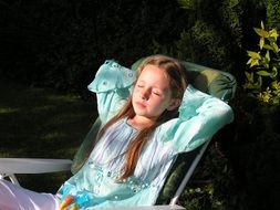 relaxed little girl on a deck chair in shadow in the garden