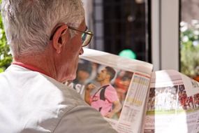 gray-haired man is reading a sports newspaper