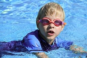 little boy with googles in the pool under the bright sun