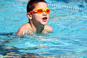 Boy with glass is swimming in the pool