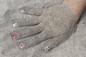 sand on child girl’s hand with manicured nails