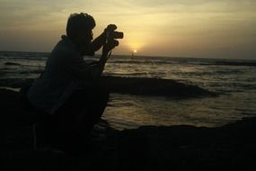man photographs sunset on the background of water