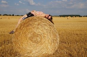 yong girl lays on her back on bale of straw on field
