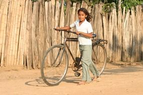 girl with a bicycle near the wooden fence