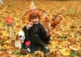 child in witch costume and hat for Halloween on the background of autumn leaves