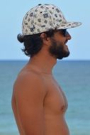 a man with a beard in sunglasses and a cap on the background of the sea