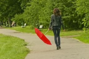 girl in black clothes walking with red umbrella in park