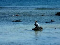 mauritian angler sits on stone among water