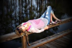 young girl laying down on wooden fence of pier at water