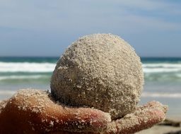 Sand ball on the hand at coast background