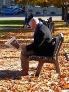 man reading a newspaper on a bench in the park