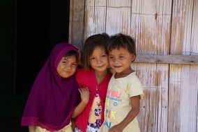 two asian child girls and boy at wooden wall, indonesia