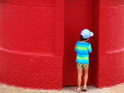 child is hiding near the red wall