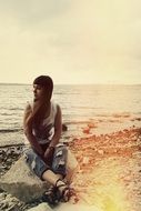 Girl is sitting on the stone near the sea