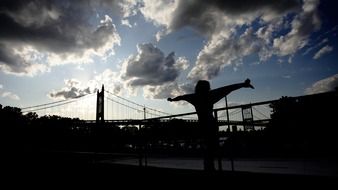 silhouette of girl in front of bridge at cloudy sky