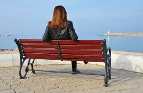 woman on bench looking at sea, back view