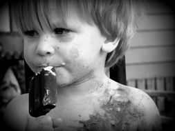 child with dirty face is eating ice cream in black and white background