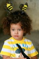 funny horns in the form of bees on the head of a blue-eyed child with curly hair