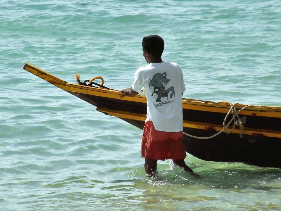 thai boy walking in water at side of fishing boat